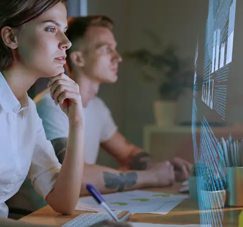 Dos personas analizan información proyectada en una pantalla transparente. Dos personas analizan información proyectada en una pantalla transparente.