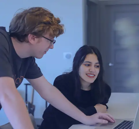 Dos personas colaboran frente a una laptop, sonrientes y concentradas.